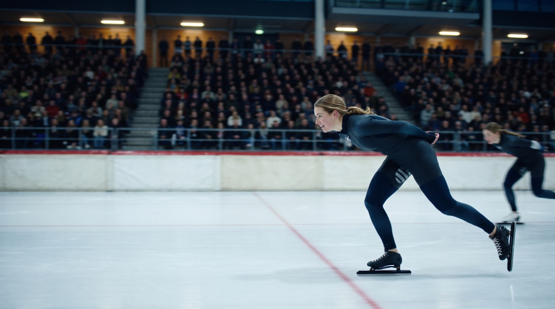 De schaatsster komt als winnaar over de finishlijn in een vol stadion, met een tweede schaatsster net achter haar